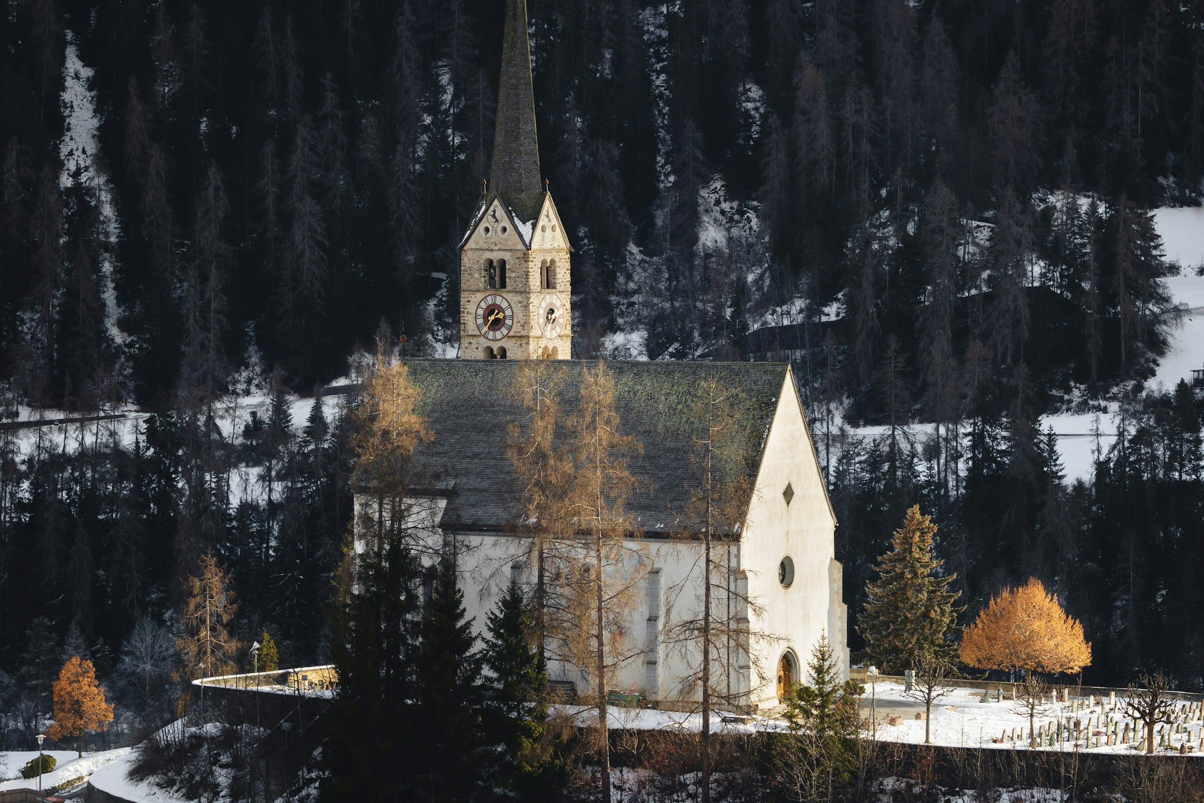 Scuol church among autumn trees and patches of snow; archive photograph by Tomas Trajan, not current conditions